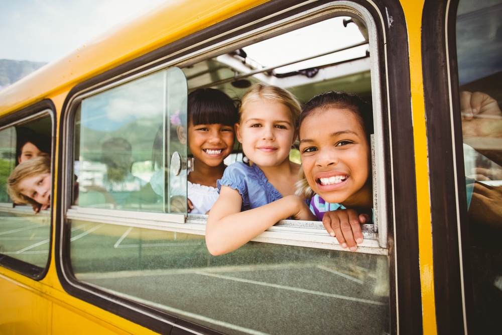 Cute pupils smiling at camera in the school bus outside the elementary school.jpeg